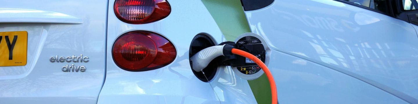Auto elettrica collegata a una stazione di ricarica, con il cavo connesso e una luce che indica il progresso della carica. Auto elettrica collegata a una stazione di ricarica, con il cavo connesso e una luce che indica il progresso della carica.