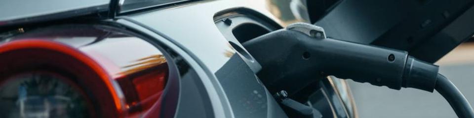 Macchine elettriche_websim4 Auto ecologica in ricarica, con il cavo attaccato e un display che mostra l’avanzamento dell’energia accumulata.