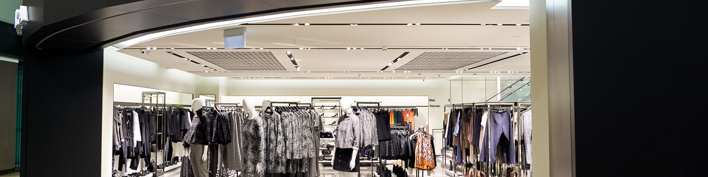 Interno di negozio di abbigliamento moderno: Spazio ben illuminato con scaffali e abiti esposti ordinatamente.