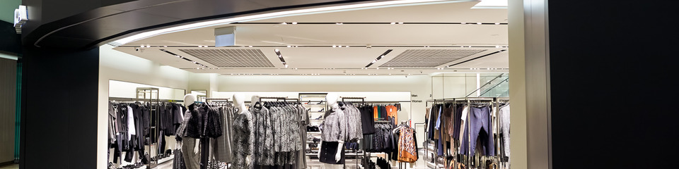 Interno di negozio di abbigliamento moderno: Spazio ben illuminato con scaffali e abiti esposti ordinatamente.