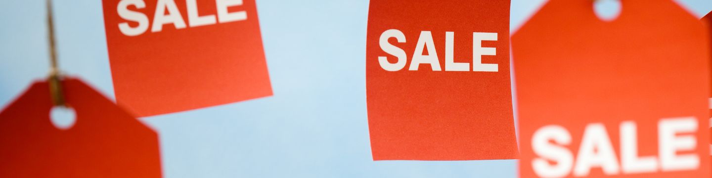 Immagine rappresentativa di cartellini rossi che penzolano dal soffitto con il testo "Sale" in primo piano di colore bianco