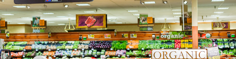  Corsie di supermercato con scaffali pieni di prodotti organizzati per categoria, illuminati da luci brillanti.  Area frutta e v