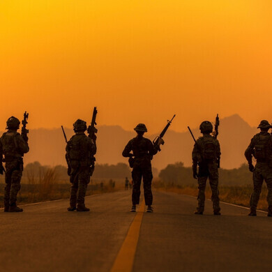 Sagome di soldati in azione sullo sfondo di un cielo arancione al tramonto, simbolo di esercito e operazioni militari.
