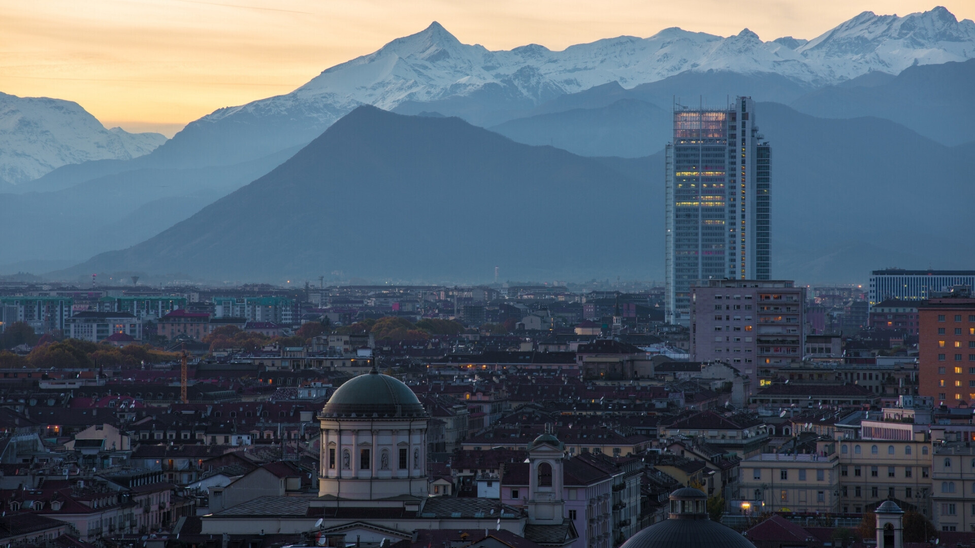 Vista dall’alto di Torino con la cupola della Chiesa di San Massimo, il grattacielo Grattacielo Intesa Sanpaolo e le Alpi innevate sullo sfondo.
