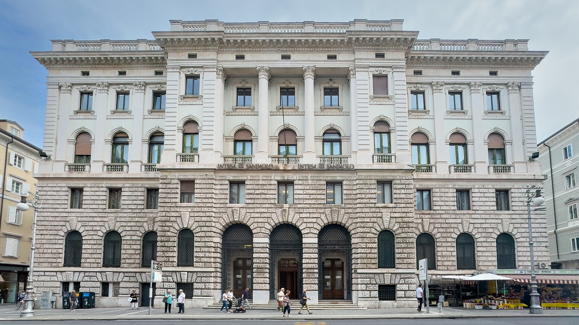 Trieste, 27 giugno 2024. Storico edificio monumentale bianco di Intesa Sanpaolo in Via Mazzini, con passanti in strada.