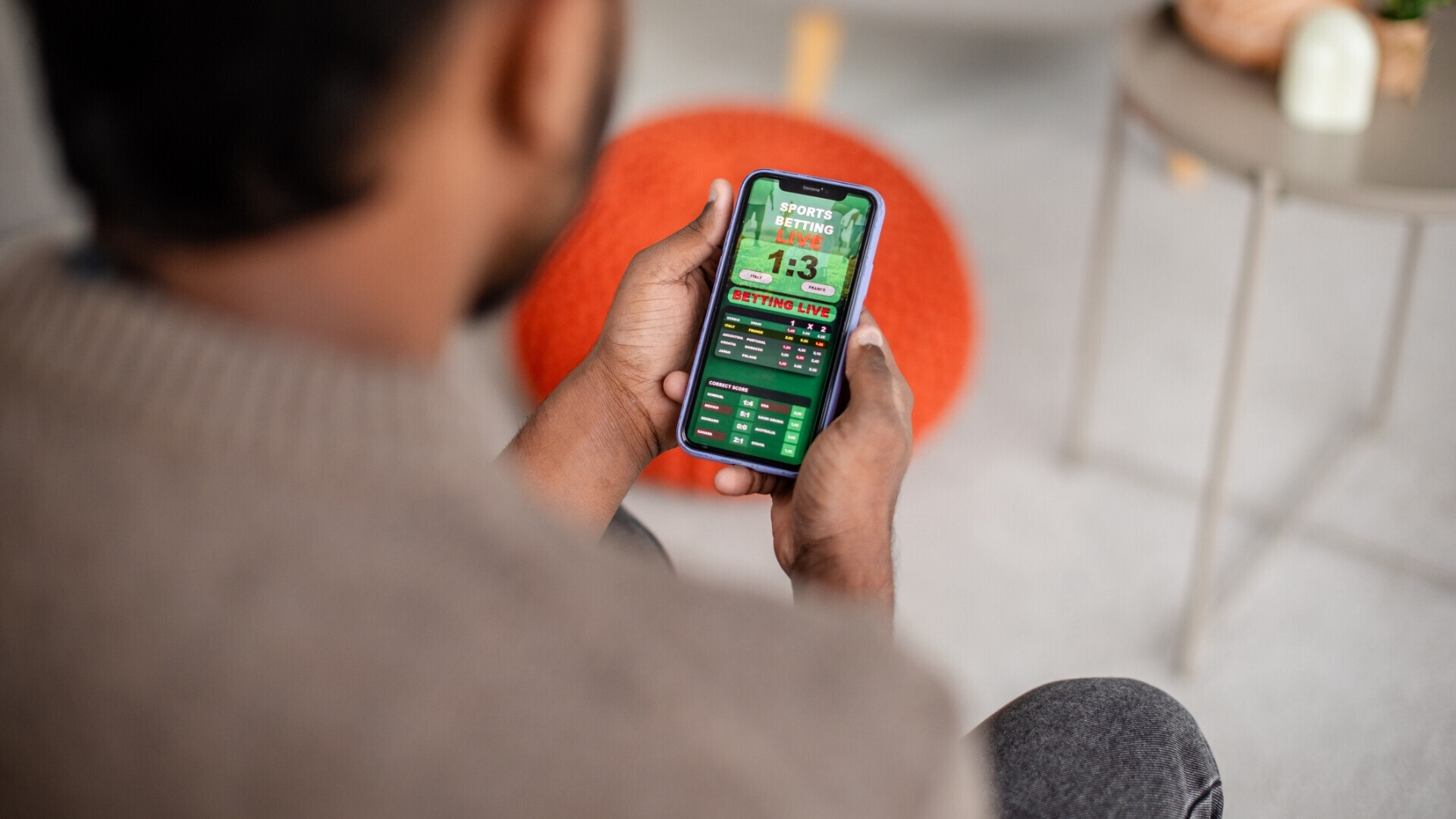 Uomo che controlla i risultati sportivi sullo schermo del dispositivo mobile Uomo concentrato mentre guarda i risultati sportivi o un gioco sullo schermo del suo smartphone, in un ambiente domestico accogliente.
