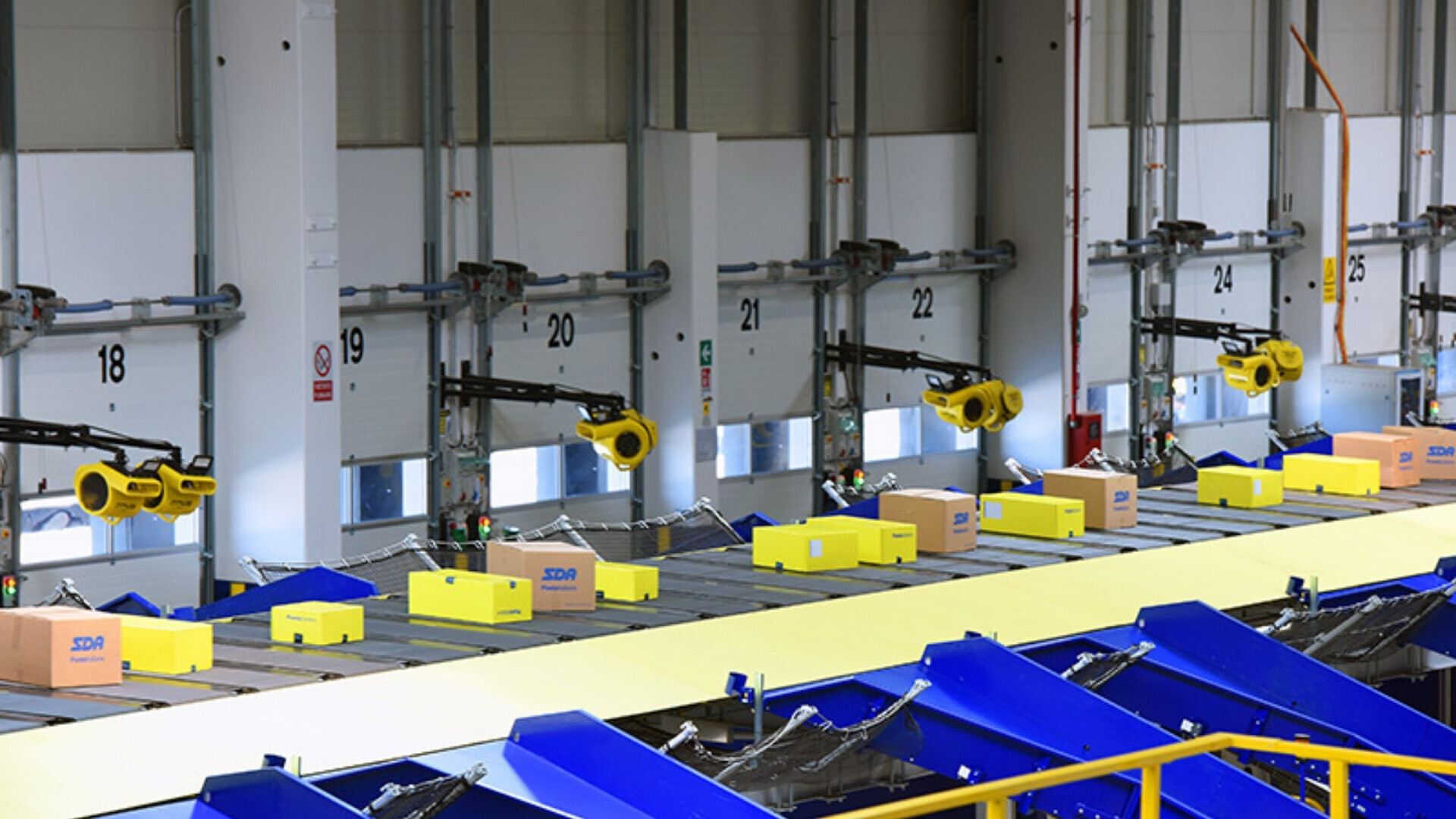 Centro logistico di Poste Italiane con nastri trasportatori e operatori impegnati nello smistamento dei pacchi.