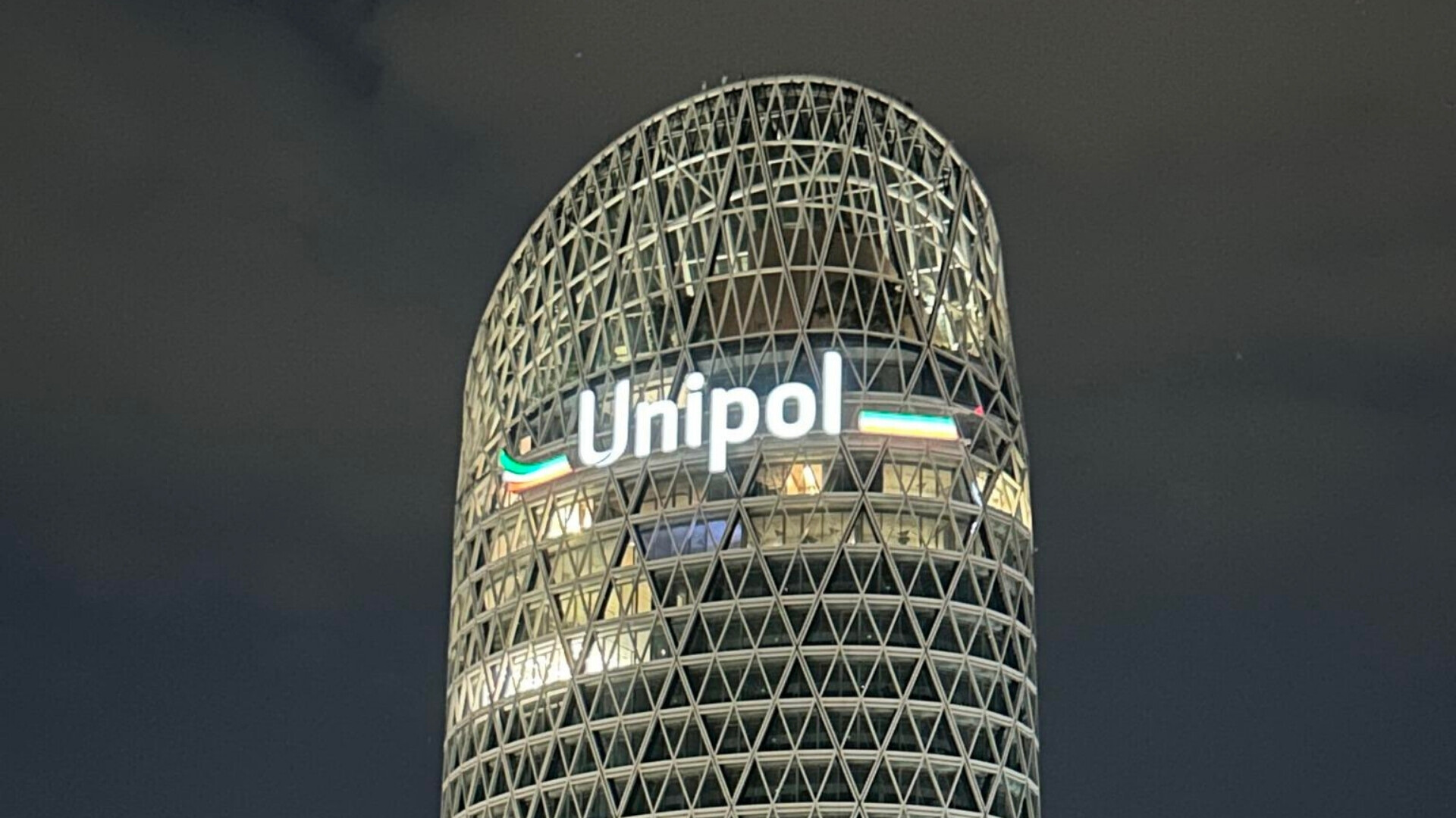 Torre Unipol a Milano illuminata di notte, con luci interne e riflessi sulle superfici in vetro.