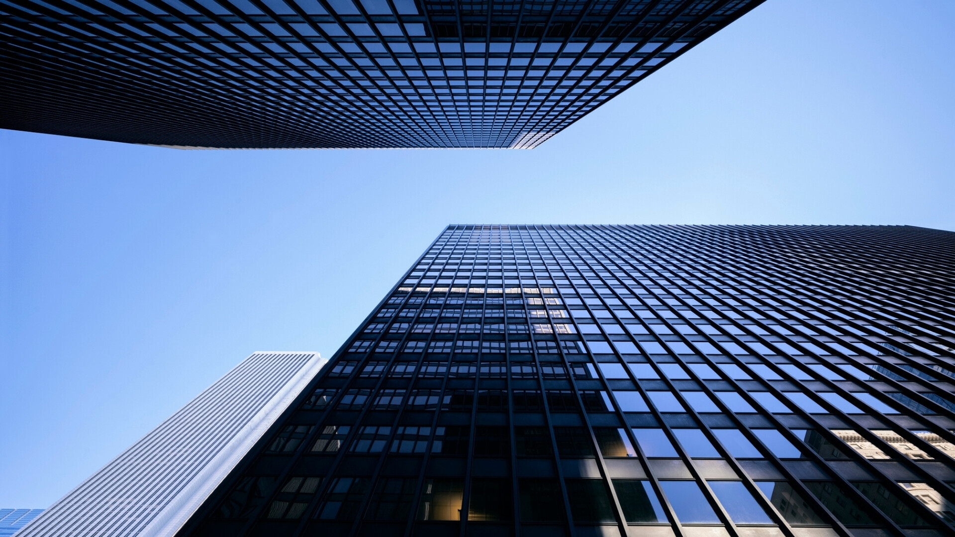 Prospettiva dal basso di moderni edifici per uffici, con facciate in vetro che riflettono il cielo azzurro in una giornata soleggiata.
