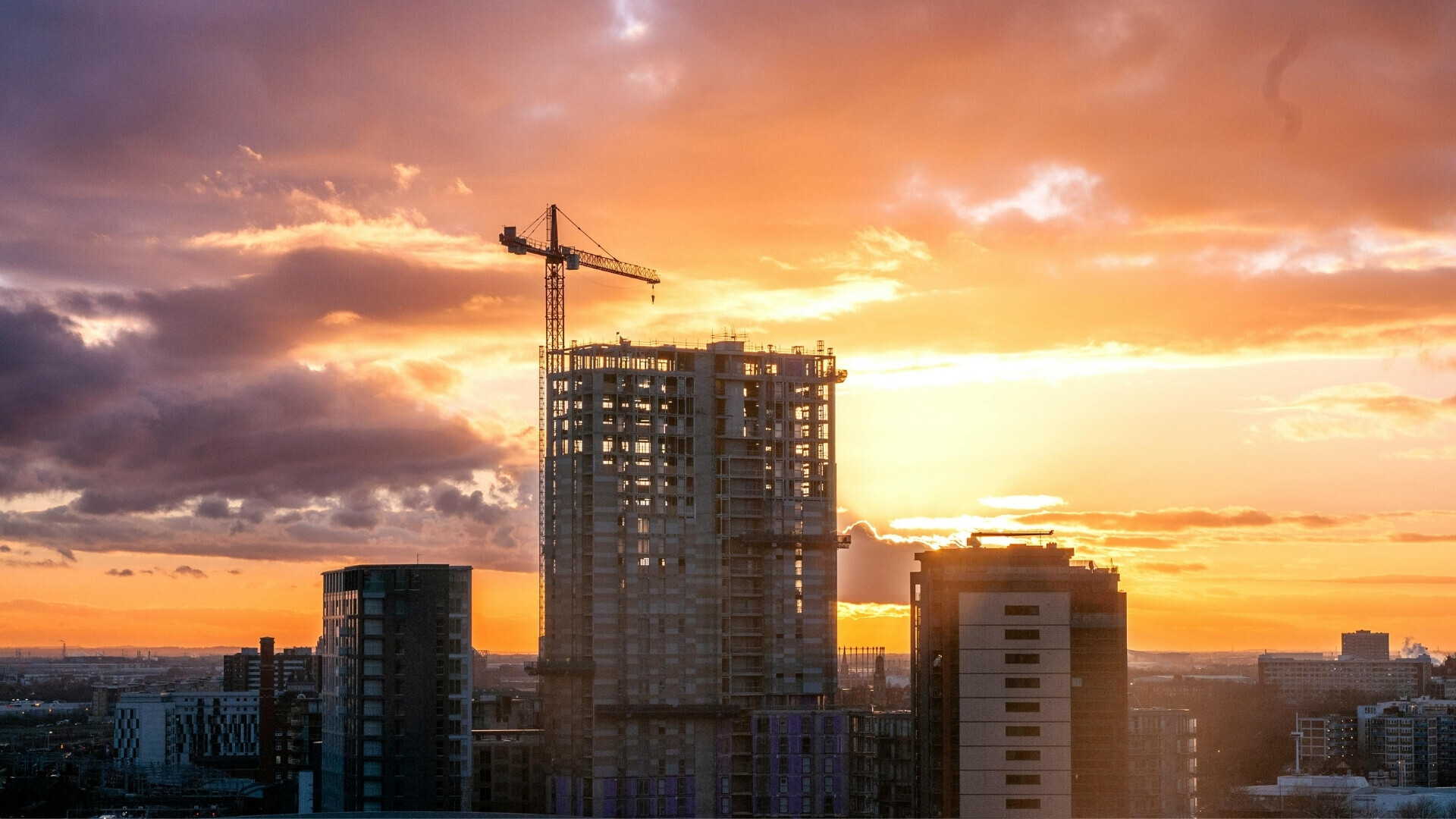 Gru e cantiere in costruzione al tramonto Strutture di impalcature metalliche illuminate dal sole al tramonto, con il cielo arancione sullo sfondo.