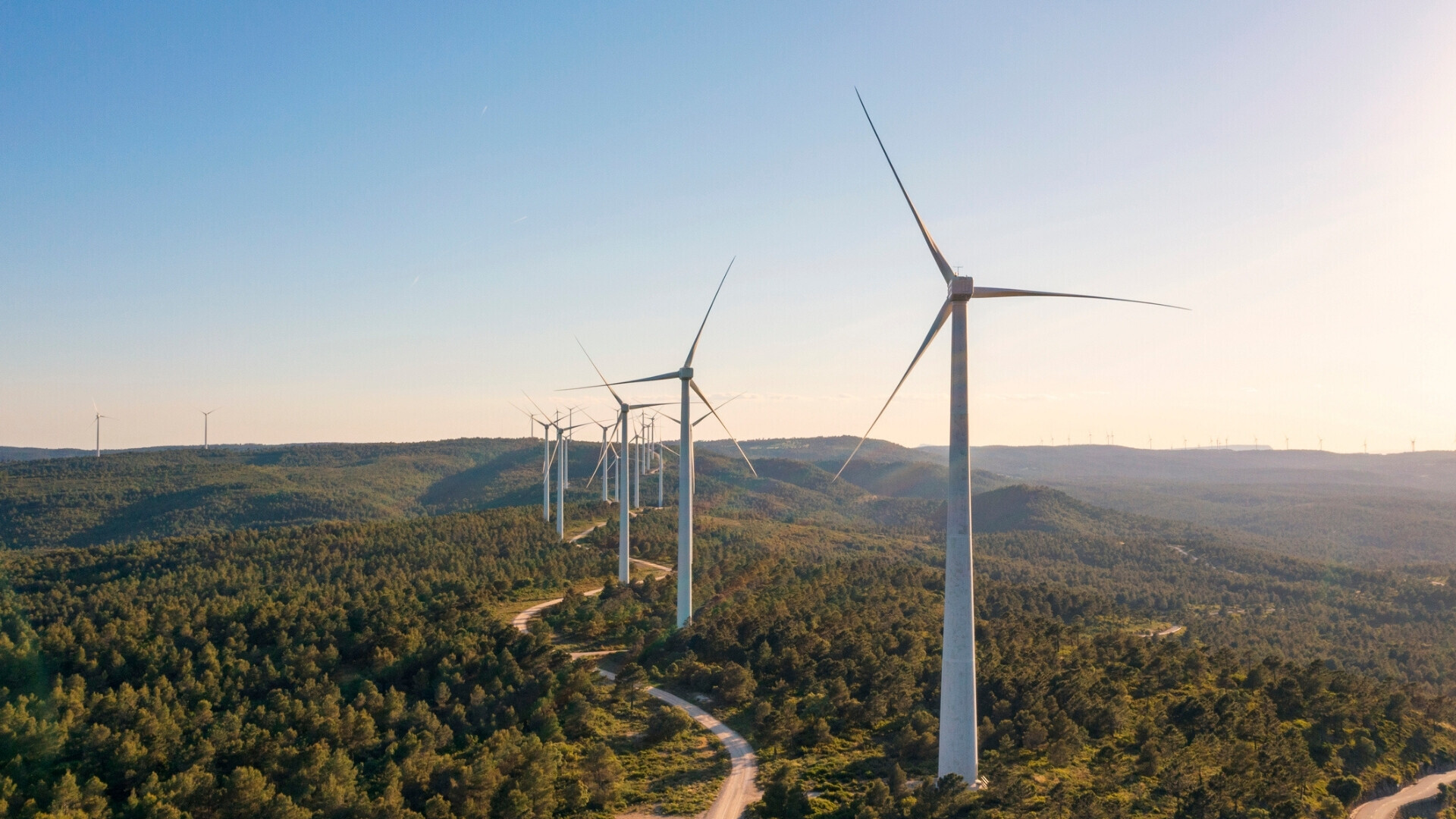 Turbine eoliche disposte in fila nella campagna spagnola, illuminate dai colori caldi del tramonto, simbolo di energia rinnovabile.