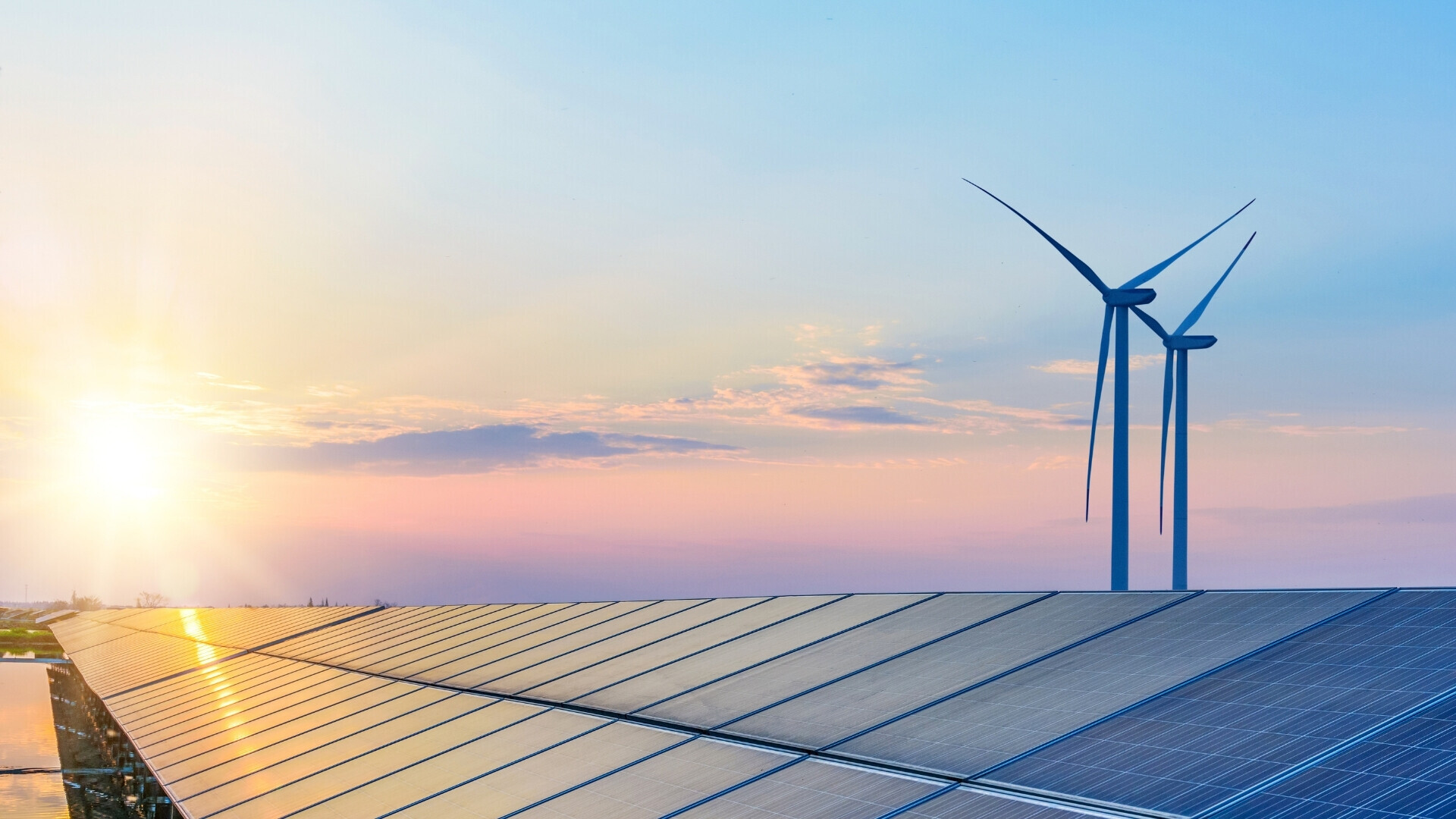 Campo di pale eoliche e pannelli fotovoltaici sotto un cielo arancione all’alba