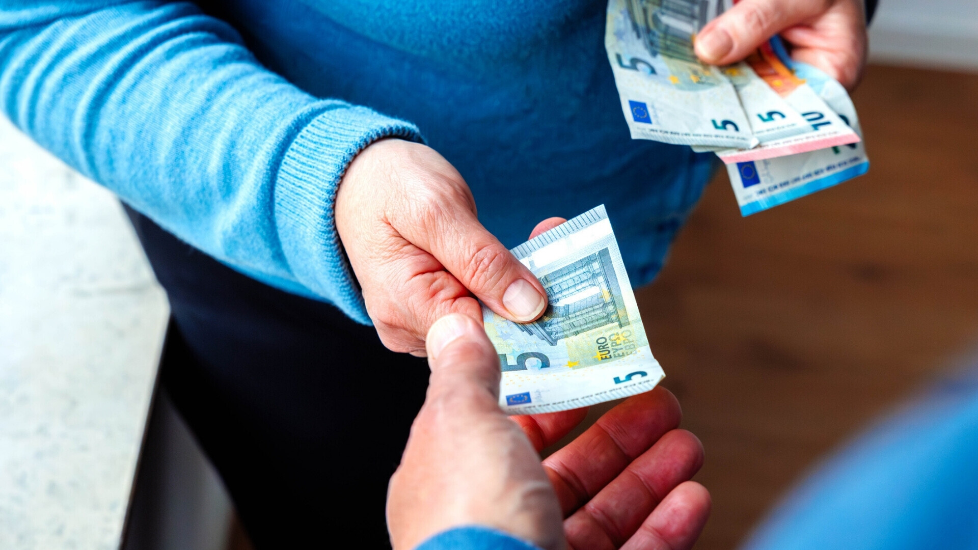 Donna che porge una banconota da 5 euro a un uomo Inquadratura oltre la spalla di una donna che consegna una banconota da cinque euro a un uomo