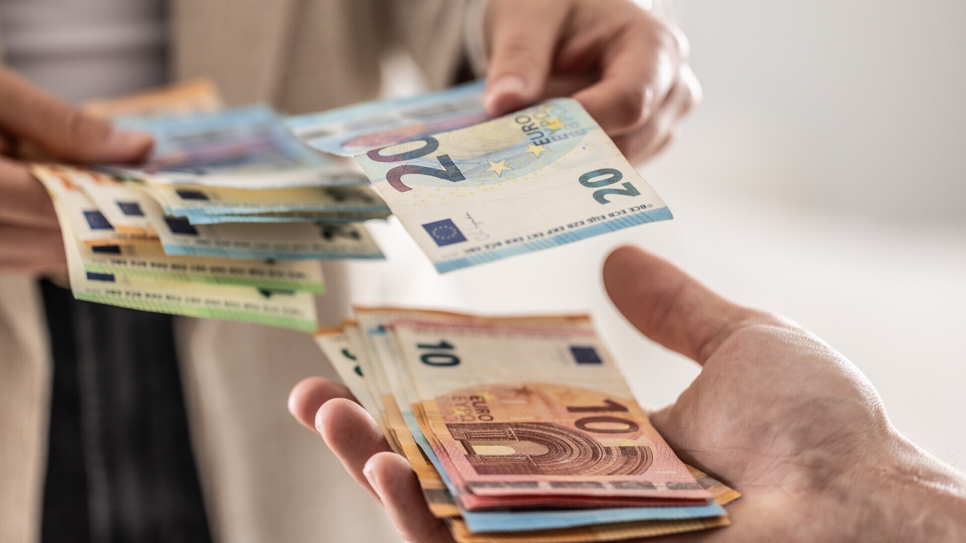 Primo piano delle mani di una donna d’affari che scambiano banconote in euro, rappresentazione di transazioni finanziarie o pagamenti.