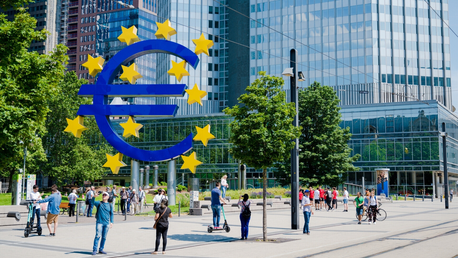 Grande scultura del simbolo dell’Euro davanti alla Banca Centrale Europea a Francoforte, Germania, con persone visibili.