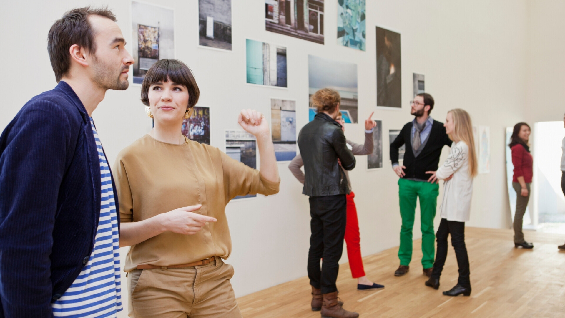 Visitatori immersi in un’esposizione fotografica, intenti a guardare le opere appese alle pareti in uno spazio espositivo luminoso.
