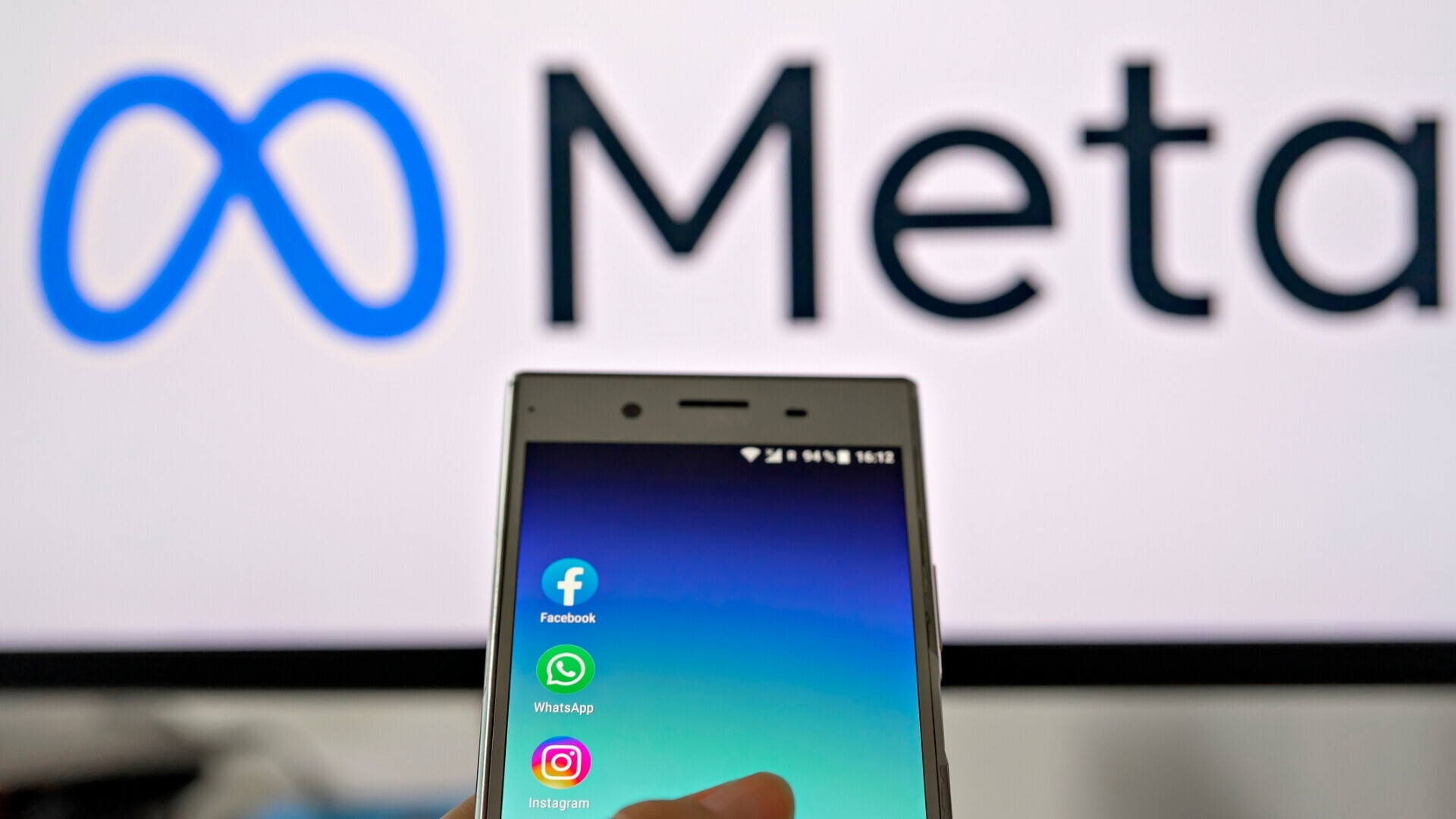 Smartphone che mostra le applicazioni meta, sullo sfondo il logo Meta