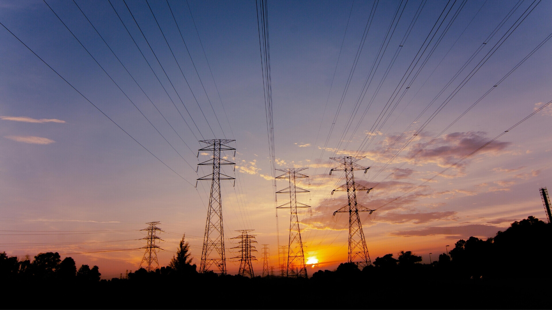 Tralicci elettrici al tramonto Torri elettriche fotografate con il sole al tramonto, che crea un contrasto tra struttura metallica e cielo colorato.